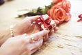 Small present box with bow in woman hands. Bracelet of pearls on hand. focus on bow. Red roses flowers behind on wooden table. Royalty Free Stock Photo