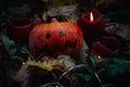 A small pumpkin with a frightening face among candles in leaves