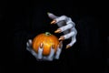 Small pumpkin in witches knotty hand. Scary undead pale fingers with long sharp claws in the dark, low key, selected Royalty Free Stock Photo