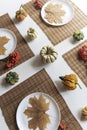 small pumpkins and dry brown maple leafs on white plates, autumn dinner table