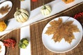 small pumpkins and dry brown maple leafs on white plates, autumn dinner table