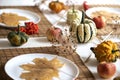 Small pumpkins and dry brown maple leafs on white plates, autumn dinner table