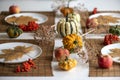 small pumpkins and dry brown maple leafs on white plates, autumn dinner table