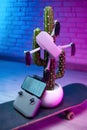 a small quadcopter drone is sitting on an artificial cactus standing on a skateboard in a neon light creative idea Royalty Free Stock Photo