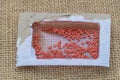 A small rectangular plastic seed packet with red seeds inside, on a burlap background