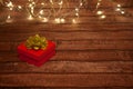 Small red box for wrapping a gift stands on a dark brown wooden background. Above the box is a decoration of a golden ribbon