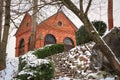 Small red brick old house on hill visible from leading down stairs with hedges covered in snow