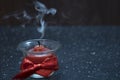 A small red candle burns in a glass bowl with a red ribbon