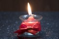 A small red candle burns in a glass bowl with a red ribbon