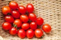 Small red cherry tomatoes spill out of a wicker basket on an old wooden table in rustic style, selective focus Royalty Free Stock Photo