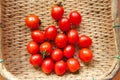 Small red cherry tomatoes spill out of a wicker basket on an old wooden table in rustic style, selective focus Royalty Free Stock Photo