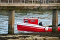 A small red fishing boat between the posts of a pier on a calm day Royalty Free Stock Photo