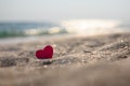 Small red heart on the sand against the background of bokeh from the glare of the sea.