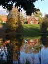 A small red house on a green hill is reflected in the mirror surface of the pond Royalty Free Stock Photo