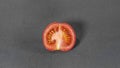 Small red tomato, cut in half and set against a backdrop of mid grey cloth Royalty Free Stock Photo