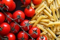 Small red tomatoes on the vine, dry penne pasta, on black wood f
