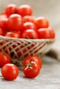 Small red tomatoes in a wicker basket on an old wooden table. Ripe and juicy cherry Royalty Free Stock Photo