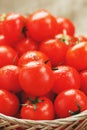 Small red tomatoes in a wicker basket on an old wooden table. Ripe and juicy cherry Royalty Free Stock Photo