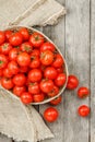 Small red tomatoes in a wicker basket on an old wooden table. Ripe and juicy cherry Royalty Free Stock Photo