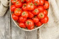 Small red tomatoes in a wicker basket on an old wooden table. Ripe and juicy cherry and burlap cloth, Terevan style country style Royalty Free Stock Photo