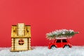 Small red toy car carrying spruse tree on a snowe road next to wooden hous. Festive christmas greeting card Royalty Free Stock Photo