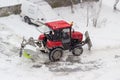 Small red tractor snow plow in courtyard during snowfall Royalty Free Stock Photo