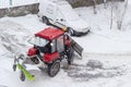 Small red tractor with snow plow in courtyard during snowfall Royalty Free Stock Photo