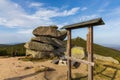 Small rest point next to mountain trail with small wooden bench and table next to huge stones and small wooden frame
