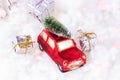 Small retro red toy car with green fir  tree on the top and presents on white artificial snow background. Christmas and New Year Royalty Free Stock Photo