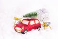 Small retro red toy car with green fir  tree on the top and presents on white artificial snow background. Christmas and New Year Royalty Free Stock Photo