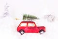 Small retro red toy car with green fir  tree on the top and presents on white artificial snow background. Christmas and New Year Royalty Free Stock Photo