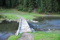 A small rickety bridge and old planks and logs, thrown over the stormy stream of the river flowing through the morning forest Royalty Free Stock Photo