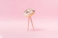 Small ring donut with white glaze and colorful crumbs with plastic model woman toy legs walking on a pink pastel background. Royalty Free Stock Photo