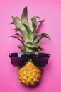 Small ripe pineapple with sunglasses on bright pink background, fashion photography top view close up