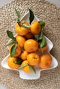 Small ripe tangerines with leaves, on plate in shape of Christmas tree on wicker serving napkin. Concept winter vitamin food.