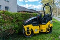 A small road-building roller of yellow-black color standing on the lawn.