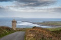 Small road leads to Doonagore castle, Doolin pier and Aran islands in the background. Beautiful cloudy sky. Popular tourist