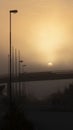 Small road with streetlights, bridge, mist and car lights in the distance. Royalty Free Stock Photo