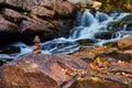 Small rock stack cairn on leaf-covered rocks along cascading river waterfalls Royalty Free Stock Photo