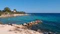 A small rocky spit forms a small bay with a warm transparent turquoise sea and stones at the bottom