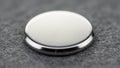 A small round silver button cell battery lies on a textured gray surface Royalty Free Stock Photo