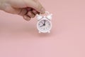 Small round white clock alarm clock keeps baby`s hand on pink background