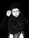 Small serious boy or cute nerd kid in glasses, hat and fashionable knitted scarf on black background.