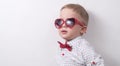 A small serious boy with glasses and a red bow tie is posing against the white wall. Royalty Free Stock Photo