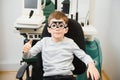 Small serious boy sitting on chair office of vision test. doctor picks up lenses to special glasses.