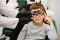 Small serious boy sitting on chair office of vision test. doctor picks up lenses to special glasses.
