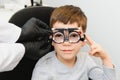 Small serious boy sitting on chair office of vision test. doctor picks up lenses to special glasses.