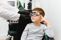 Small serious boy sitting on chair office of vision test. doctor picks up lenses to special glasses.