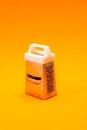 A small shiny metal grater isolated on orange background, close-up of cheese and food stainless grater. Vertical orientation