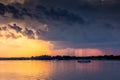 A small ship is sailing along the river against the backdrop of the sunset. Rain clouds in the sky